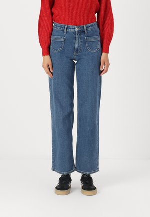 Jeans in denim blu a gamba larga con vita alta, dotati di due tasche frontali e orlo sfilacciato, abbinati a sneaker nere con suola in gomma.