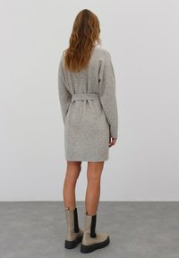 Grau gestricktes Kleid mit einem Taillenbund, langen Ärmeln und gerippten Bündchen. Kombiniert mit beigen Ankle Boots mit schwarzen Seitenpanelen.