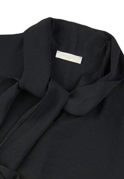 Blusa nera con colletto annodato, realizzata in tessuto setoso. Presenta un'etichetta cucita all'interno del collo. Texture liscia e caduta fluida.