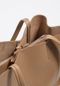 Torebka tote w kolorze tan z fakturowanym wykończeniem, z dwiema rączkami i zamknięciem na zamek, z zamszowym wnętrzem.