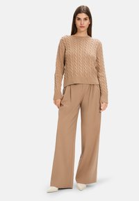 Beiger Strickpullover mit Rundhals und langen Ärmeln, kombiniert mit weiten beigen Hosen und spitzen cremefarbenen Heels.