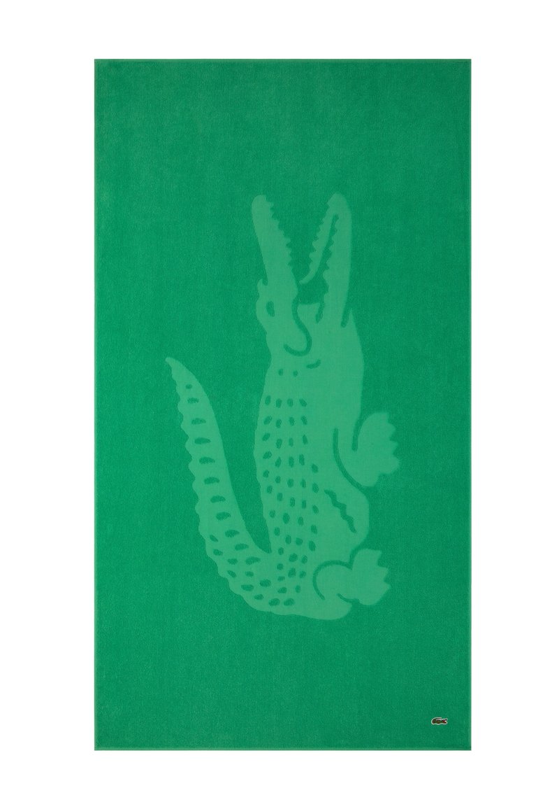 Alfombra de algodón verde con un gran diseño sutil de cocodrilo. Textura suave con un tejido grueso y un pequeño logo en la esquina.