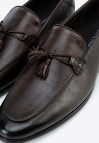 Tmavě hnědé kožené mokasíny s hladkým povrchem, s akcentem v podobě třásní a elegantním zaobleným špičatým designem.