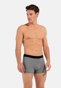 Boxer shorts neri con vita elastica, caratterizzati da un motivo geometrico grigio, tessuto elastico e design aderente. I pantaloni corti hanno una lunghezza a metà coscia e una texture liscia.