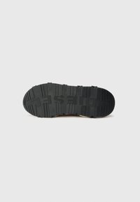 Semelle de chaussure en caoutchouc noir avec un motif texturé, présentant des rainures et le mot "DESERT" en relief. Forme de bout circulaire, design plat.