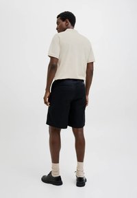 Polo beige, pantaloni corti neri e scarpe nere. Maniche corte e colletto classico sulla polo, con una texture di tessuto liscia.