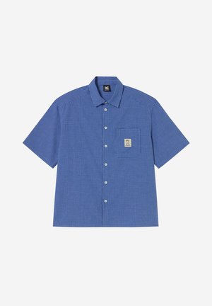 Camicia blu a maniche corte con piccoli motivi a quadretti e tasca frontale con toppa quadrata beige con un logo.