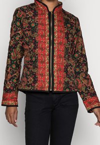 Gequilted jack met een zwarte basis en rood-gouden paisleypatronen, afgewerkt met een zwarte rits en een mandarinaanzit.