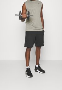 Gray sleeveless athletic top, black shorts, and black sneakers with white accents. Holding a dumbbell, standing on a neutral background.