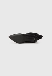 Bottines noires en tissu avec un bout pointu et une semelle texturée. Matériau doux, froncé autour de la cheville. Design élégant et look minimaliste.