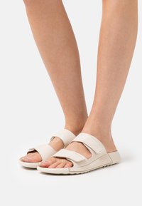 Infradito beige chiaro con due larghe cinghie regolabili, design aperto sulla punta e suola testurizzata per una presa sicura. Materiale liscio con accenti minimi.