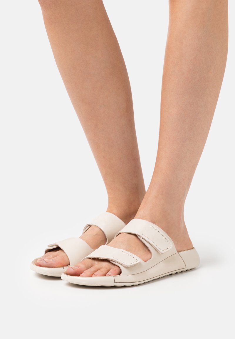 Infradito beige chiaro con due larghe cinghie regolabili, design aperto sulla punta e suola testurizzata per una presa sicura. Materiale liscio con accenti minimi.