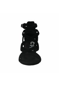 Zwarte suède hoge hak sandalen met gekruiste banden, sluiting met gespsluiting rond de enkel en een open teen ontwerp. Getextureerd oppervlak, gedurfde branding aan de binnenkant.