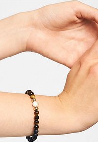 Perlenarmband mit schwarzen matten und polierten Steinen, das ein zentrales Goldton-Detail mit kreisförmigem Design aufweist. Sichtbare strukturierte Oberfläche.