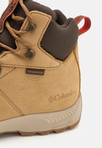 Tan waterproof hiking boot with brown textile accents, lace-up design, reinforced toe cap, and textured gray outsole featuring the Columbia logo.