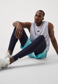 Sportkleding met een lichtgrijze mouwloze shirt en teal shorts over marineblauwe leggings. Sneakers zijn wit met grijze accenten.