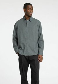 Grijze blouse met een subtiel patroon, lange mouwen en een zachte textuur, gecombineerd met zwarte broek. Bevat een klassieke kraag en knopen aan de voorkant.