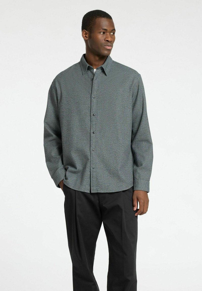 Grijze blouse met een subtiel patroon, lange mouwen en een zachte textuur, gecombineerd met zwarte broek. Bevat een klassieke kraag en knopen aan de voorkant.