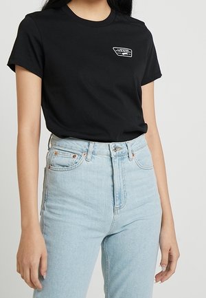 Schwarzes Baumwoll-T-Shirt mit einem weißen Vans-Logo-Patch, kombiniert mit hellblauen, hoch taillierten Jeans. Einfaches Rundhalsausschnitt-Design.