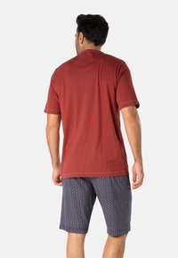 T-shirt bordeaux à manches courtes avec un col rond, associé à un short gris à motifs géométriques. Tissu en coton doux.