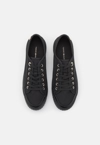 Paar schwarze Low-Top-Sneaker mit schwarzen Schnürsenkeln und goldenen Ösen, die markierten Einlagen tragen die Aufschrift "Tommy Hilfiger", präsentiert auf einem weißen Hintergrund.