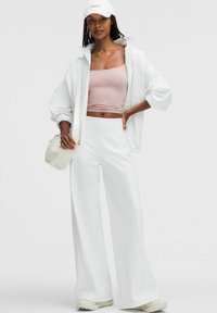 White zip-up jacket, light pink crop top, wide-leg white pants, and white cap. The outfit features a smooth texture and casual design.