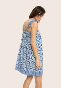 Niebieska i biała sukienka w wzory z dopasowanym tyłem, paskami na ramionach, rozkloszowanym kształtem i ozdobnym dołem.