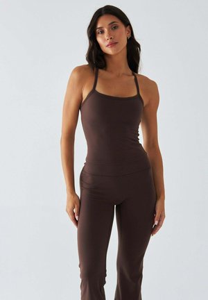 Brązowy bezrękawnik na cienkich ramiączkach oraz dopasowane legginsy w tym samym kolorze. Wykonane z elastycznego materiału, cechują się gładką fakturą i przylegającym krojem.