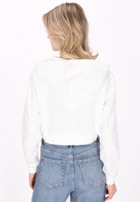 Weißer, kurz geschnittener Hoodie mit Kapuze, weicher Textur, langen Ärmeln und geripptem Saum, kombiniert mit hellblauen, hoch geschnittenen Jeans mit Taschen.