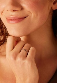 Zilveren ring op de rechterhand, rustend op de kin. Vloeiende textuur, ronde vorm, weerkaatsend licht tegen een warme huidtint.