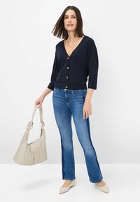 Navy V-hals cardi met gouden knopen, driekwartmouwen, gecombineerd met lichtblauwe wijde jeans en beige hakken; met een lichtbeige handtas.