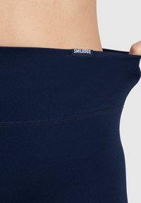 Granatowe legginsy bezszwowe o gładkiej fakturze i miękkim pasie z białą metką. Zbliżenie podkreśla elastyczny materiał.
