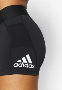 Černé sportovní šortky s vysokým pasem, obsahující strukturovaný panel a bílé logo Adidas na boku. Hladký, přiléhavý design.