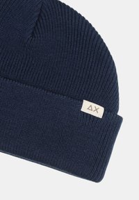 Cappello di lana blu navy con design a risvolto, con un piccolo etichetta in tessuto chiaro con i simboli ΔX. La texture è a coste.