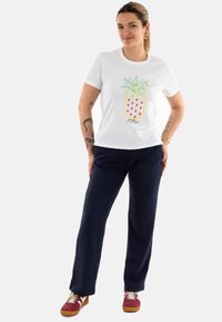 Camiseta blanca de algodón con un diseño colorido de piña, combinada con pantalones azul marino y zapatillas rojas con acentos beige.