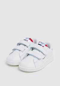 Valged sünteetilisest nahast tennisetossud, millel on kaks Velcro rihma, perforatsioonid ja logo keelel; lame kummist talla.