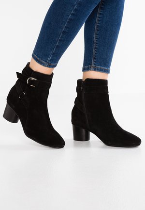 Czarne zamszowe botki za kostkę z noskiem w szpic, masywnym obcasem i ozdobnymi klamrami. Zapinane na suwak z boku dla łatwego zakładania.