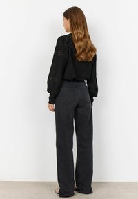 Black eyelet blouse with puff sleeves, paired with high-waisted dark gray wide-leg jeans. Smooth fabric with minimal detailing.