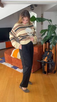 Jeune femme ajustant son pull à motifs debout dans un salon avec un rameur et une grande plante verte à proximité.