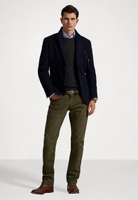 Blazer azul marino, suéter gris, camisa azul claro, pantalones de pana verde, zapatos de cuero marrón. El blazer tiene bolsillos y un corte entallado.