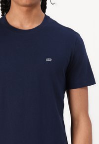 Mørkeblå bomullstrøye med rund hals og korte ermer, med en liten brodert "GAP"-logo på brystet. Glatt tekstur.