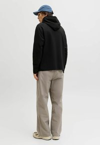 Sweat à capuche noir avec cordon de serrage, pantalon beige et chaussures beiges. Une casquette bleu clair vient compléter la tenue. Design minimaliste aux lignes épurées.