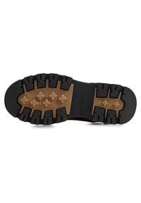 Suela negra con tacos profundos y robustos y una entresuela marrón texturizada. Presenta un detalle central de marca y una construcción resistente para tracción.