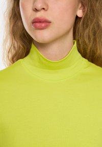 Long-sleeve, high-collared top made of ribbed fabric in vibrant neon yellow; smooth texture with a fitted design.