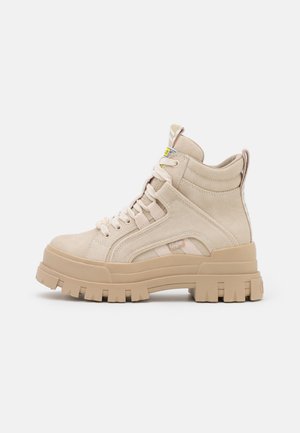 Sneaker alto beige in suede con suola spessa, caratterizzato da un design con lacci, accenti laterali e colletto imbottito.