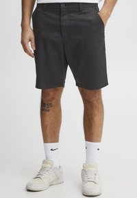 Sorte shorts lavet af glat stof, med knaplukning, lommer og en afslappet pasform. Båret med hvide sokker og sneakers.