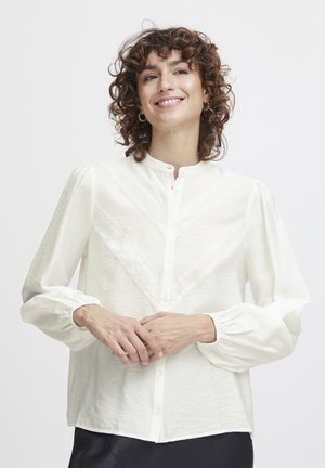 White button-up blouse with textured fabric, high neckline, and long puff sleeves. Features lace detailing in a chevron pattern.