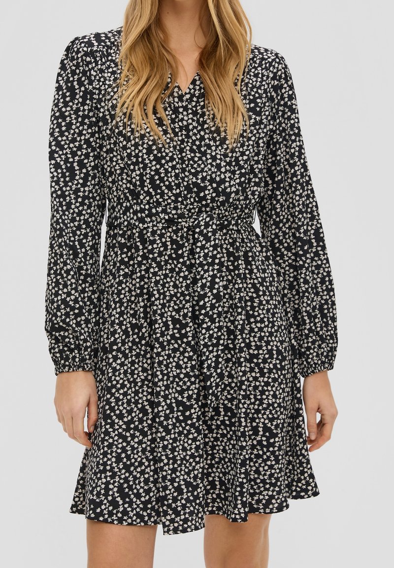 Černé květinové šaty s nařaseným pasem, dlouhými nabíranými rukávy a malým vzorem bílých květin. Volná sukně se mírně rozšířeným lemem.