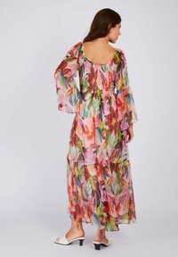 Maxi dress in sheer, colorful floral print with long, flowing sleeves. Smocked bodice and tiered skirt detail. White block-heel mules.