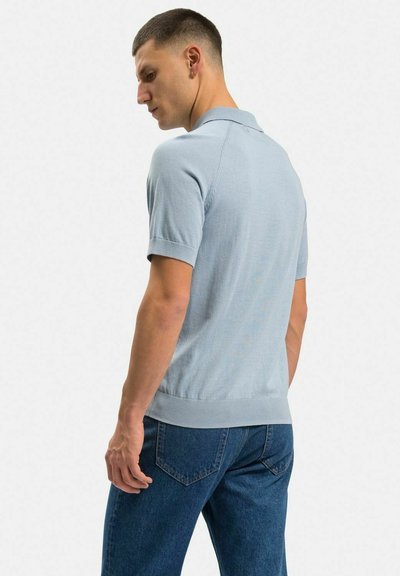 Ljusblå kortärmad polo med krage, texturerad tyg, ribbad nederkant och sömlös axeldesign, i kombination med mörkblå jeans.